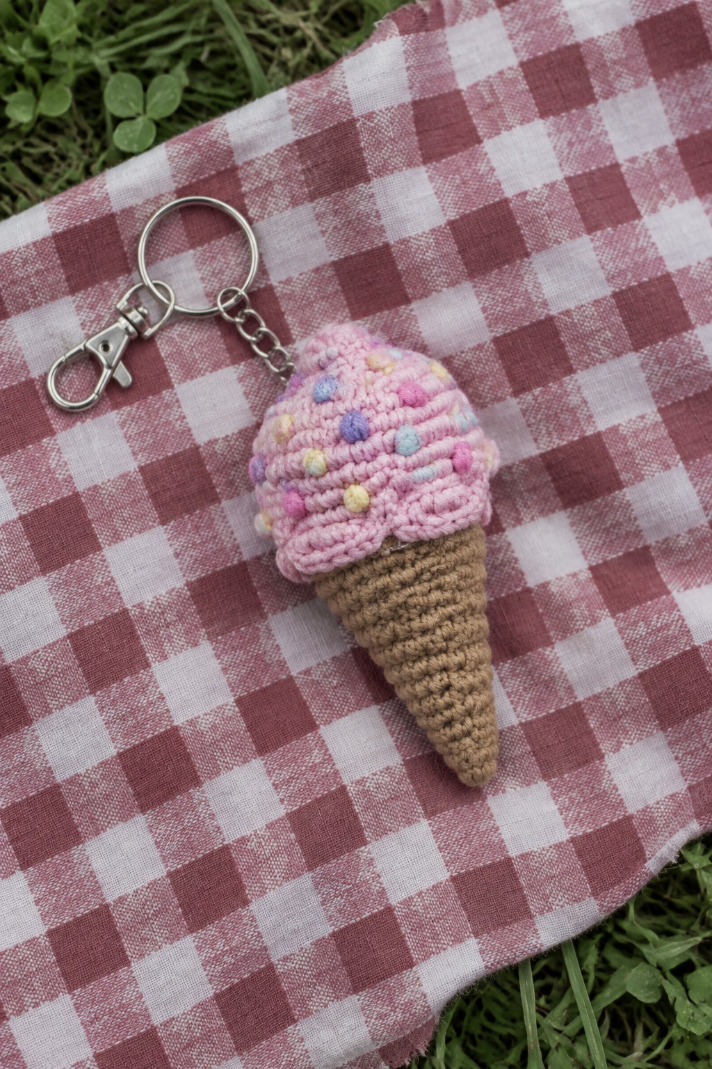 Crocheted pink ice cream cone keychain on red checkered fabric outdoors