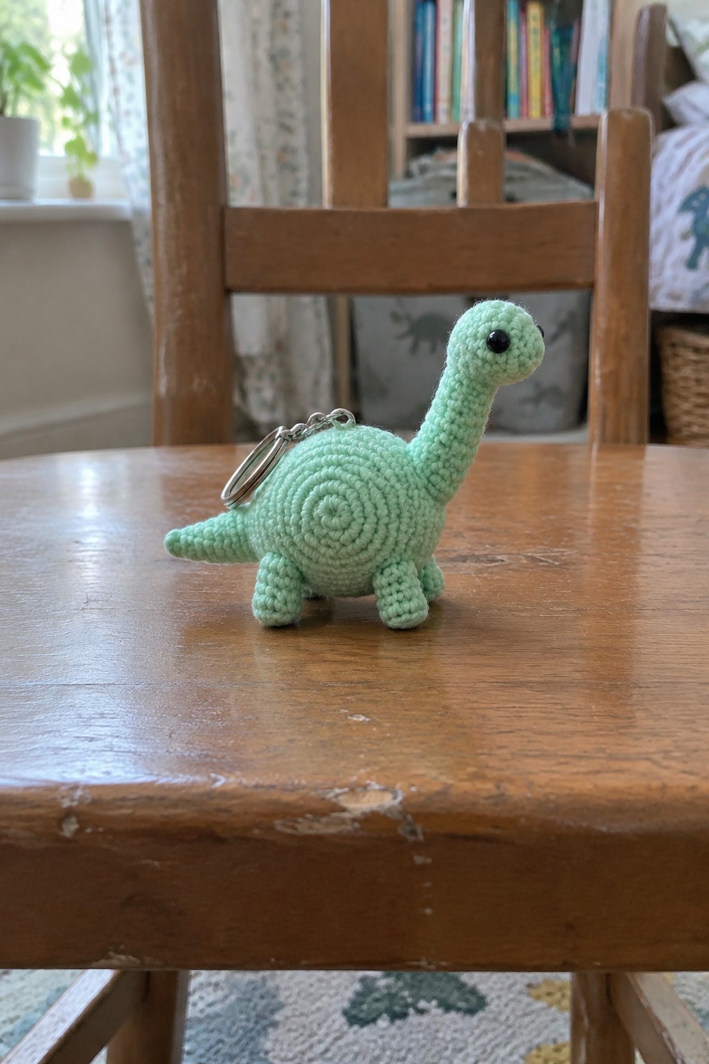 Mint green crocheted dinosaur keychain with ring on wooden table surface
