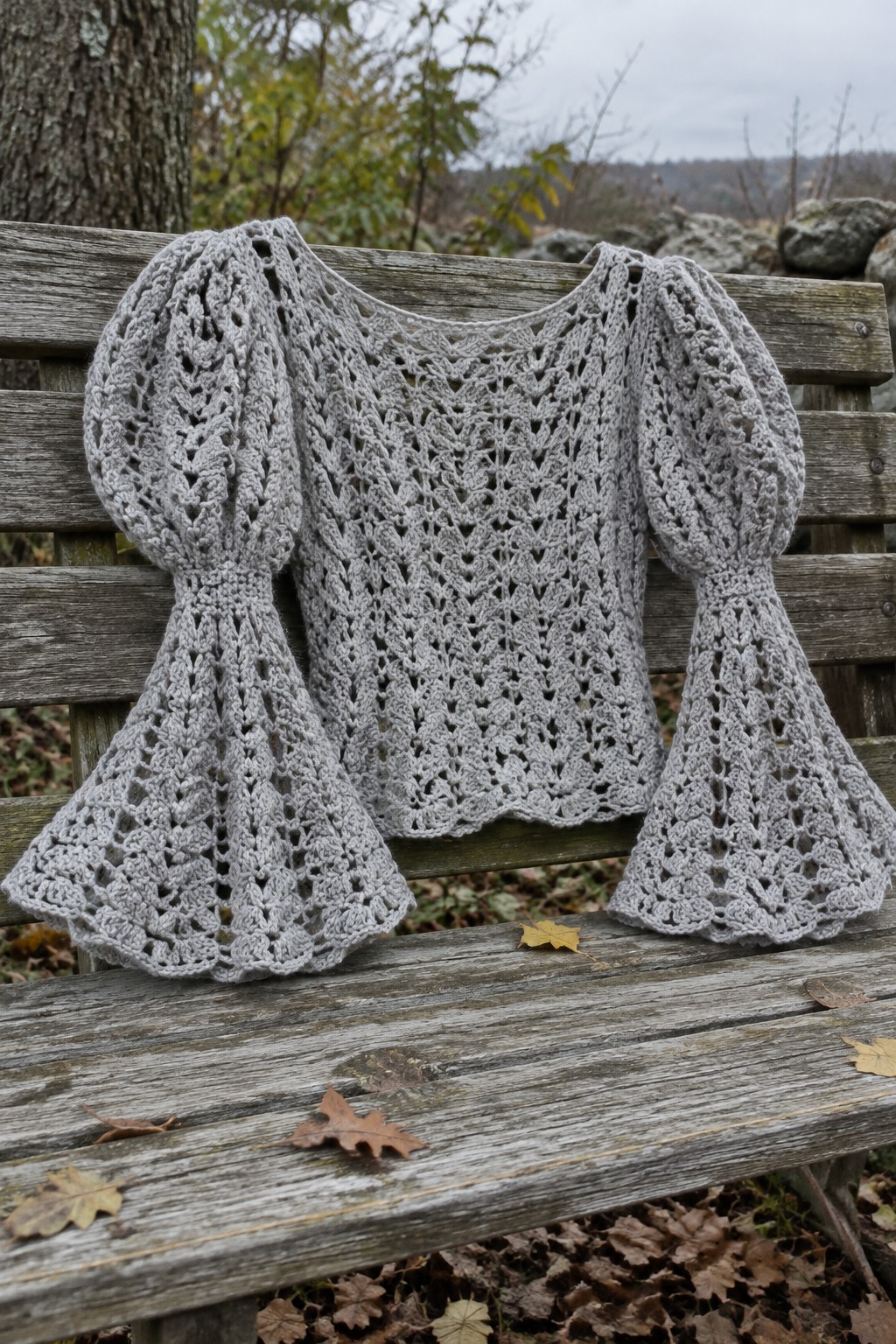Gray crocheted lace top with puffy flared sleeves on rustic wooden bench in autumn.