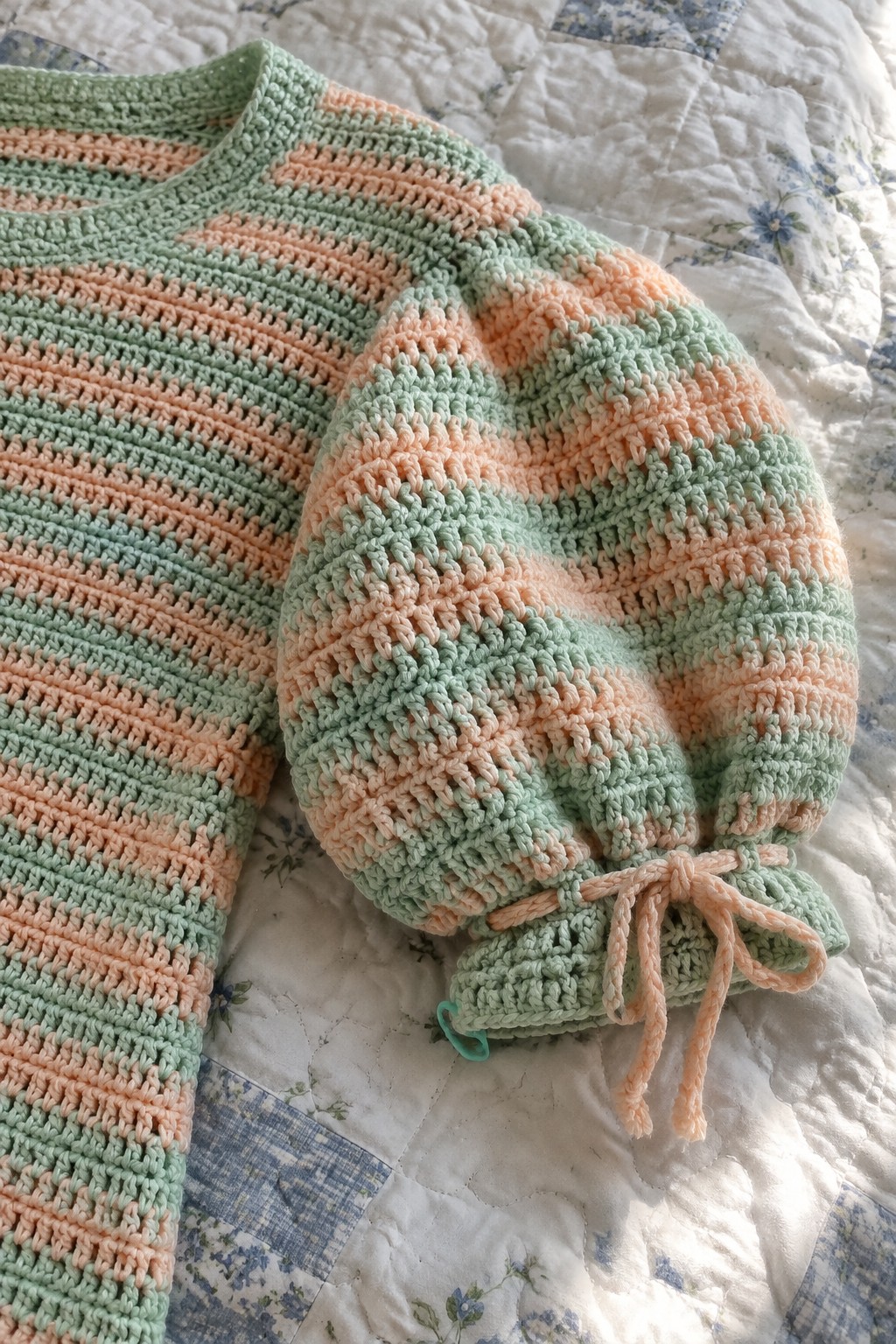Pastel striped crochet sweater with puffy sleeve and drawstring cuff on quilt