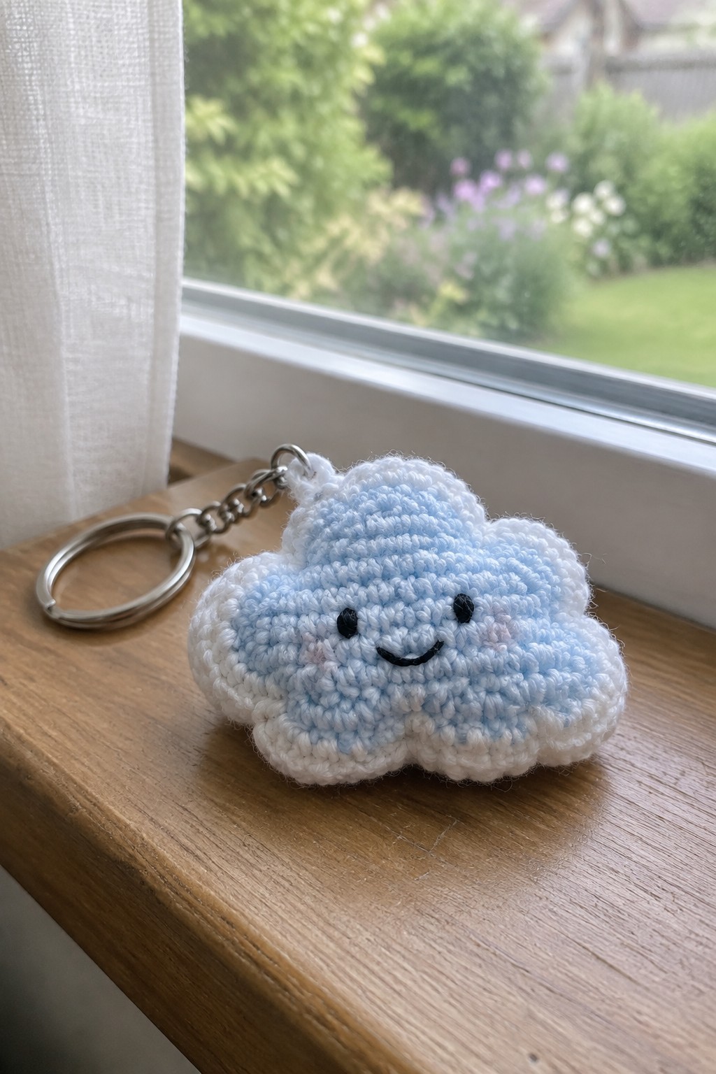 Light blue crocheted cloud keychain with smiling face on wooden windowsill