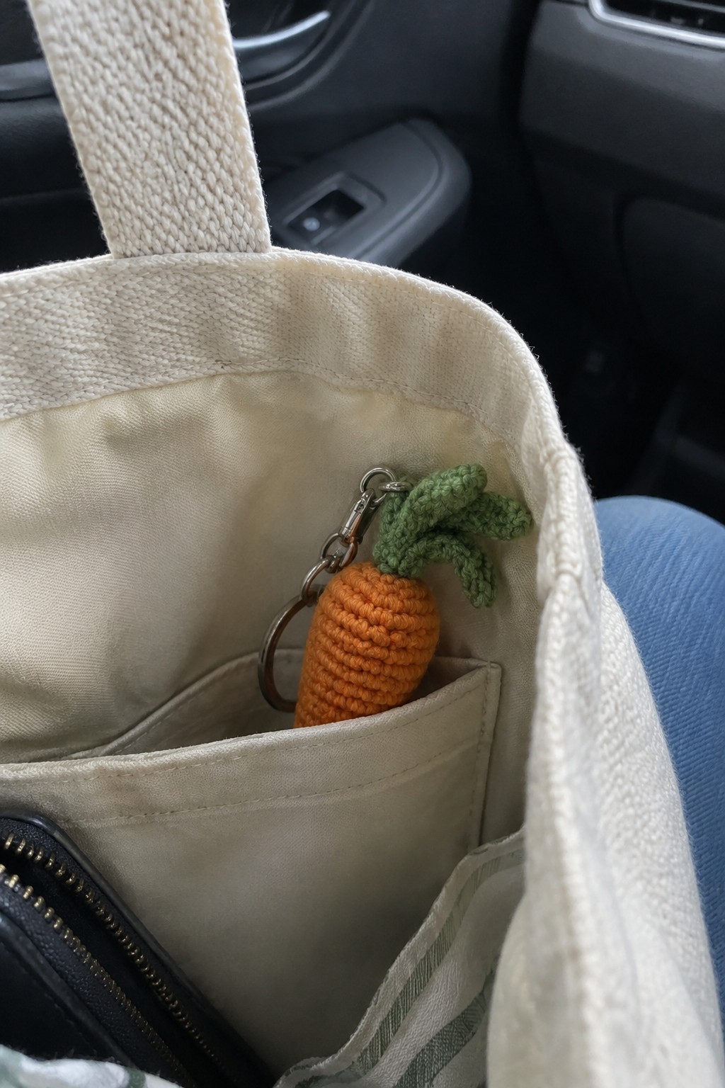 Crocheted orange carrot keychain clipped to pocket of cream canvas tote bag in car