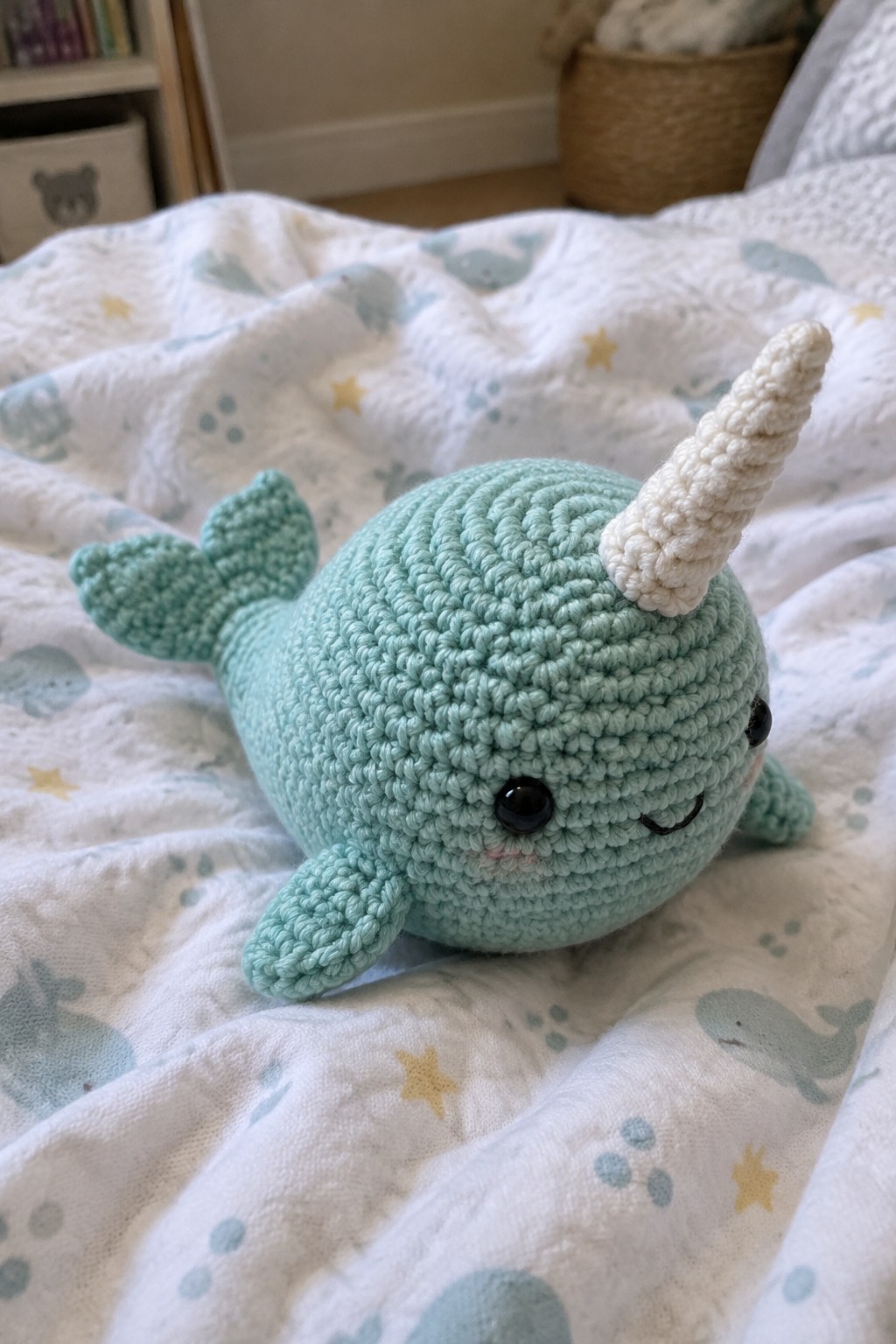 Crocheted mint green narwhal toy with white horn on patterned blanket