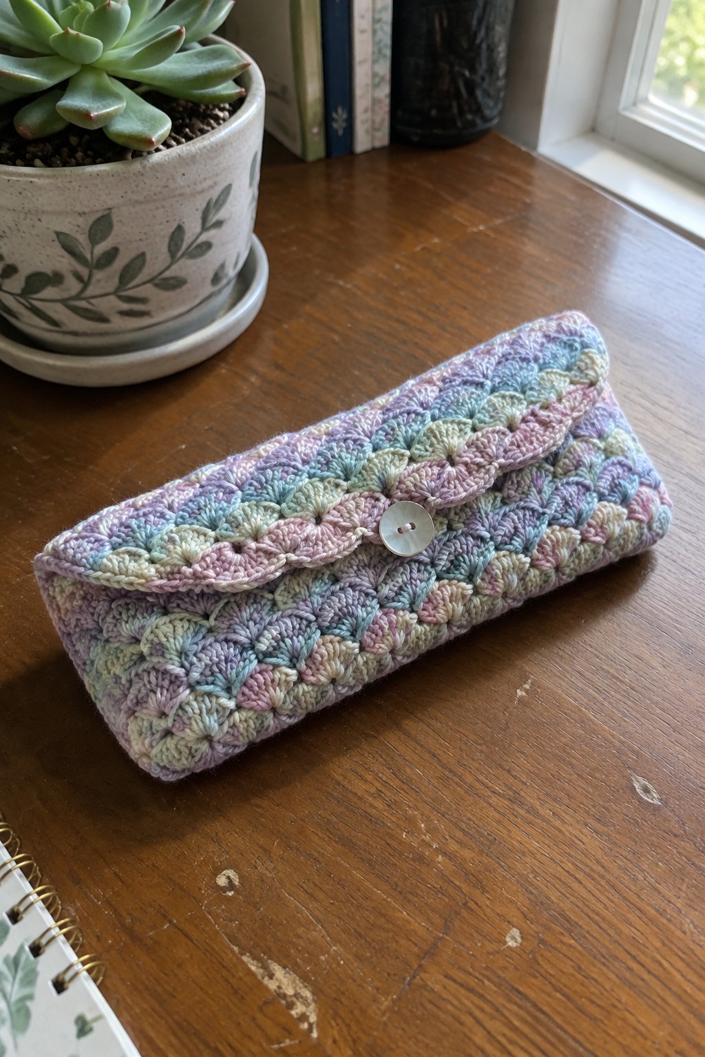 Pastel crocheted clutch with scalloped flap and button on wooden table beside plant
