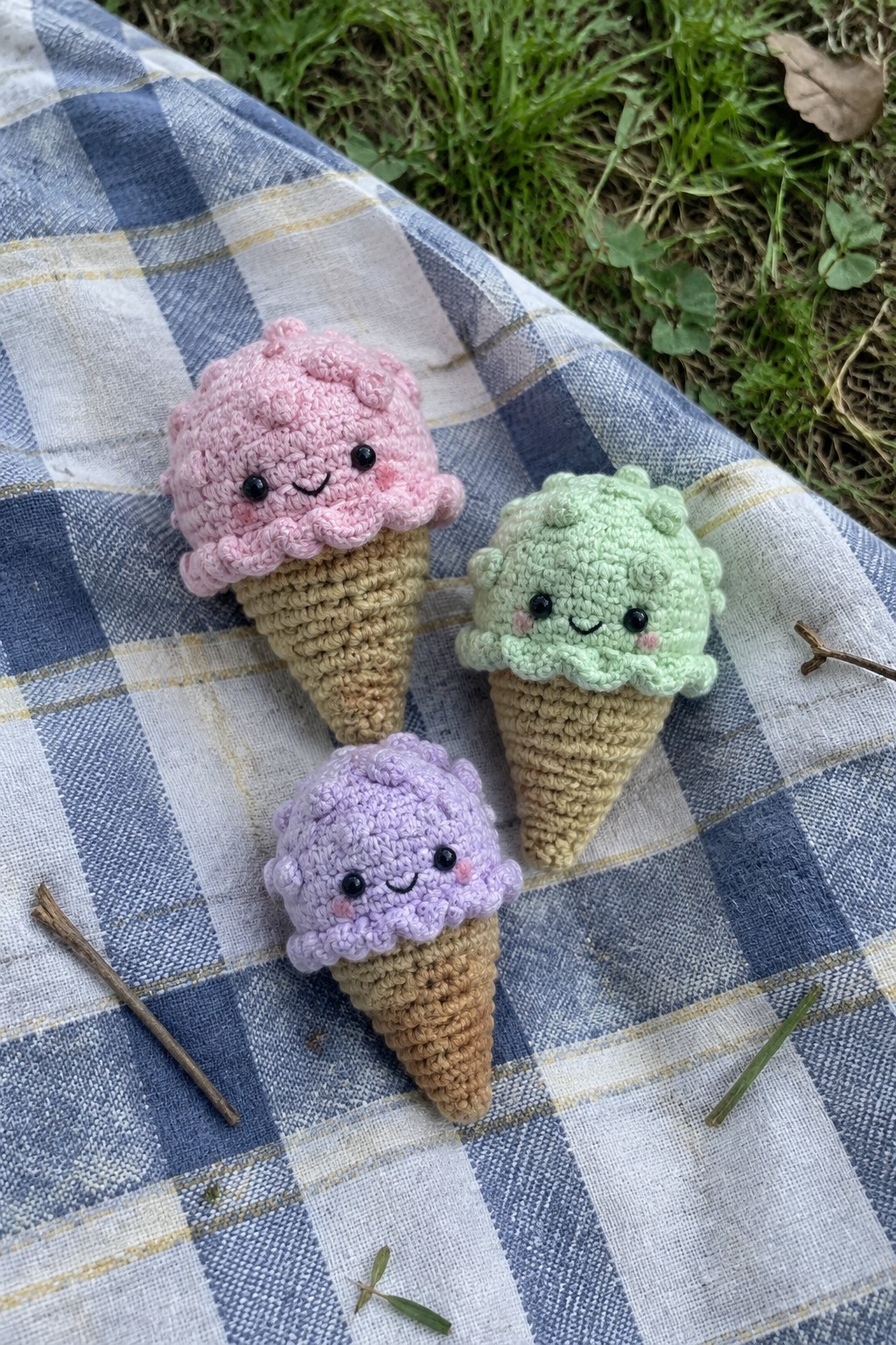 Three colorful crocheted ice cream cones with faces on checkered picnic blanket