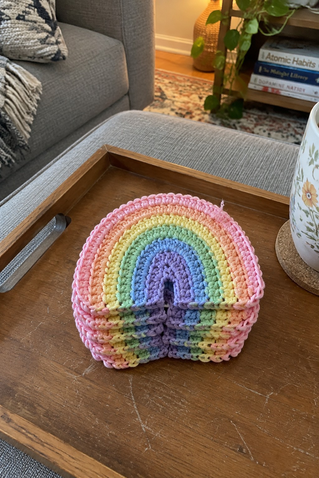 Rainbow crocheted pouch with colorful stripes on wooden tray in living room.